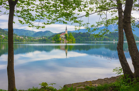 Beautiful morning at Lake Bled and Julian Alps in the background, with natural frame. The lake island and charming little church are famous tourist attraction in Slovenia.の写真素材