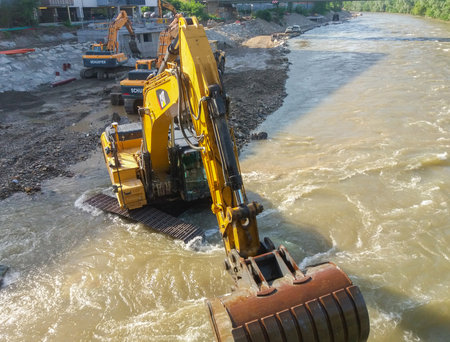 Graz/Austria - June 12, 2019: Yellow CAT industrial excavator working in the river, extracting sand and pebbles on construction siteのeditorial素材