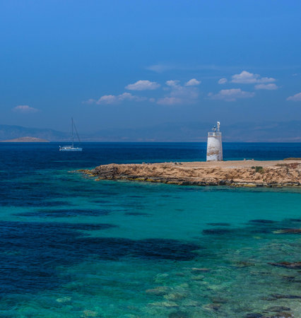 The wild coast of Aegina island with clear and blue waters of Mediterranean sea and the old small lighthouse in the background, in Saronic gulf, Greece.の写真素材