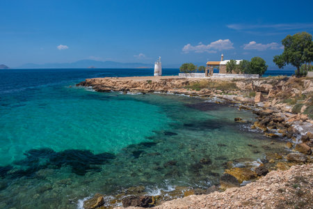 The wild coast of Aegina island with clear and blue waters of Mediterranean sea and the old small lighthouse in the background, in Saronic gulf, Greece.の写真素材