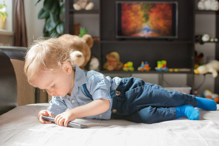 Cute baby boy playing with the remote control on a couch in the living room at homeの写真素材