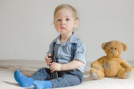 Cute baby boy and his teddy bear watching TV sitting on a couch in the living room at homeの写真素材