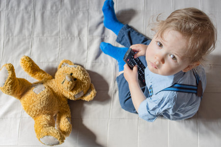 Cute baby boy and his teddy bear watching TV sitting on a couch in the living room at home, top viewの写真素材