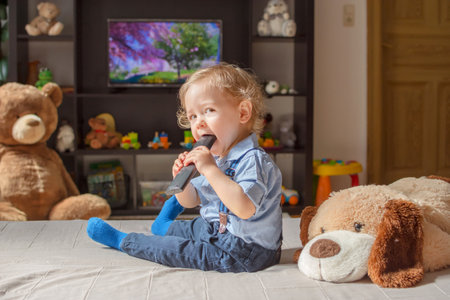Cute baby boy and his dog plush toy watching TV sitting on a couch in the living room at homeの写真素材