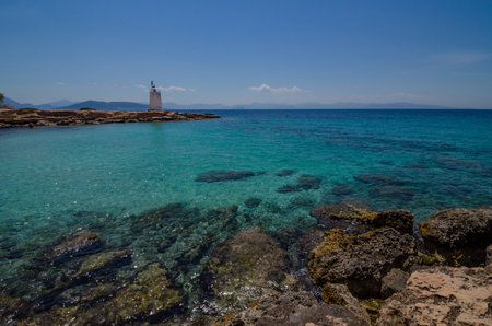 The wild coast of Aegina island with clear and blue waters of Mediterranean sea and the old small lighthouse in the background, in Saronic gulf, Greece.の写真素材