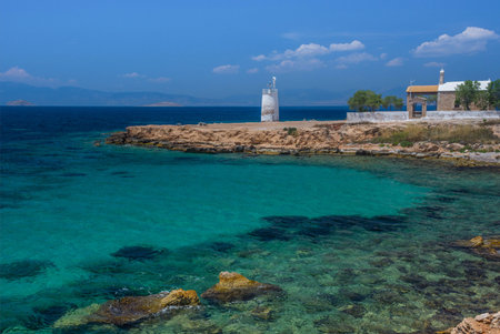 The wild coast of Aegina island with clear and blue waters of Mediterranean sea and the old small lighthouse in the background, in Saronic gulf, Greece.の写真素材