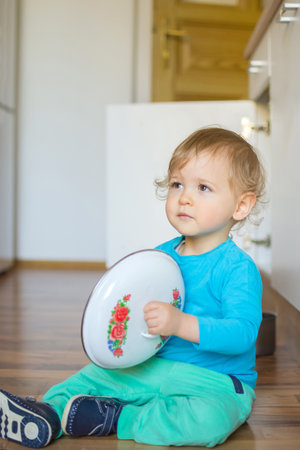 Cute little boy sitting on the kitchen floor playing with cooking pots and making a lot of noiseの写真素材