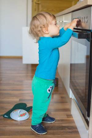Small and curious child playing with the knobs of the oven in the kitchen. Danger for unattended children, accident prevention at home conceptual photoの写真素材