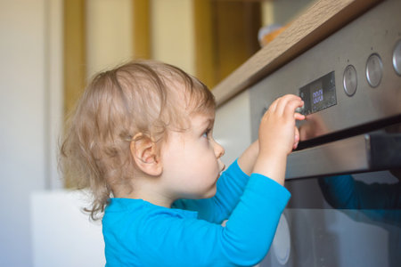 Small and curious child playing with the knobs of the oven in the kitchen. Danger for unattended children, accident prevention at home conceptual photoの写真素材