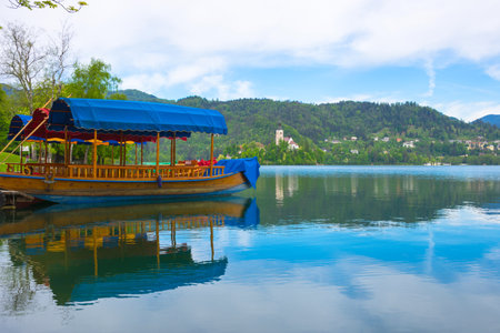 Traditional Pletna boat waiting for tourists on Lake Bled, with the lake island and charming little church in the background, famous tourists attraction in Sloveniaの写真素材