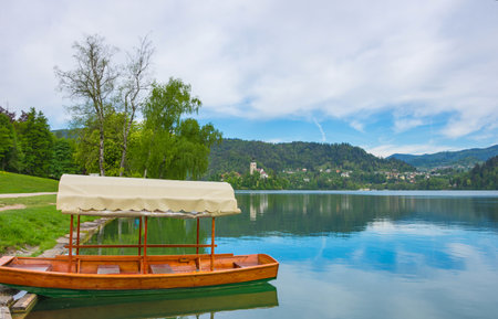 Traditional Pletna boat waiting for tourists on Lake Bled, with the lake island and charming little church in the background, famous tourists attraction in Sloveniaの写真素材