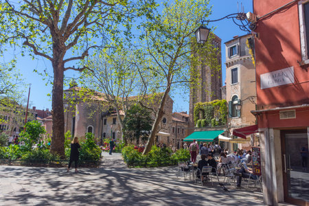 Venice, Italy - April 20, 2019: Beautiful square with terraces, restaurants and old church, in a beautiful sunny day.の写真素材