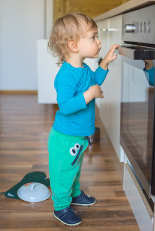 Small and curious child playing with the knobs of the oven in the kitchen. Danger for unattended children, accident prevention at home conceptual photoの写真素材