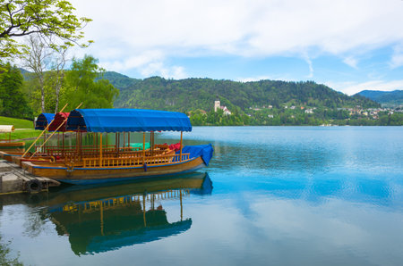 Traditional Pletna boat waiting for tourists on Lake Bled, with the lake island and charming little church in the background, famous tourists attraction in Sloveniaの写真素材