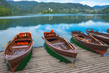 Traditional boats waiting for tourists on Lake Bled, with the lake island and charming little church in the background, famous tourists attraction in Sloveniaの写真素材