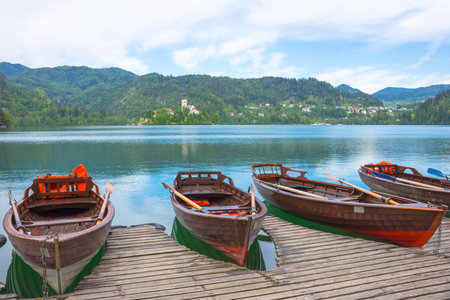 Traditional boats waiting for tourists on Lake Bled, with the lake island and charming little church in the background, famous tourists attraction in Sloveniaの写真素材