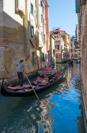 Venetian canal with tourists in the gondola among boats and historic houses, in a beautiful sunny day.の写真素材