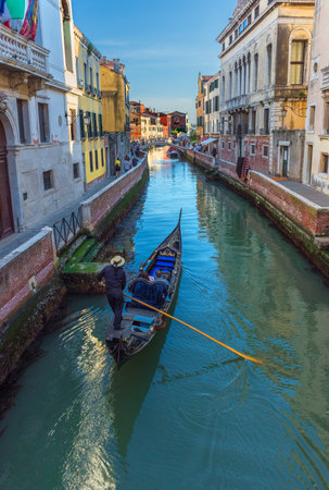 Venetian canal with tourists in the gondola among boats and historic houses, in a beautiful sunny day.の写真素材