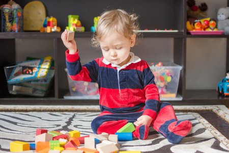 Cute little baby boy having fun at home playing with colorful wooden blocks, on the floor.の写真素材