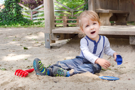 Cute little child having fun playing with sand and colorful toys in the park, beautiful summer sunny day in children playgroundの写真素材