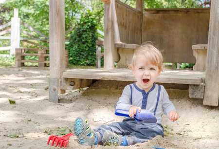 Cute little child having fun playing with sand and colorful toys in the park, beautiful summer sunny day in children playgroundの写真素材