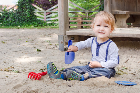 Cute little child having fun playing with sand and colorful toys in the park, beautiful summer sunny day in children playgroundの写真素材