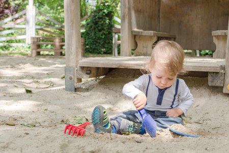 Cute little child having fun playing with sand and colorful toys in the park, beautiful summer sunny day in children playgroundの写真素材