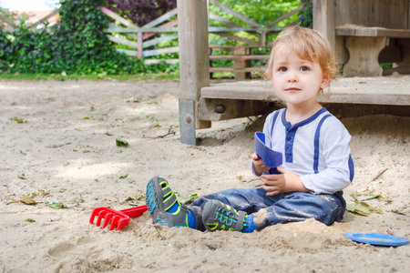 Cute little child having fun playing with sand and colorful toys in the park, beautiful summer sunny day in children playgroundの写真素材