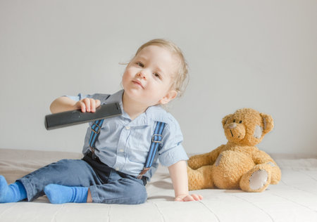 Cute baby boy and his teddy bear watching TV sitting on the floor covered with toys, at homeの写真素材