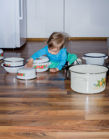 Cute little boy sitting on the kitchen floor playing with cooking pots and making a lot of noiseの写真素材