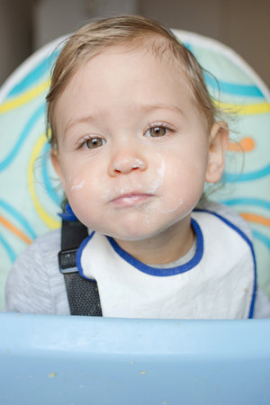 Cute baby child portrait getting messy eating cereals or porridge by itselfの写真素材