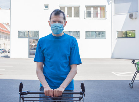 Man wearing a medical mask standing with an shopping cart in front of a store during coronavirus Covid-19 pandemic.の写真素材