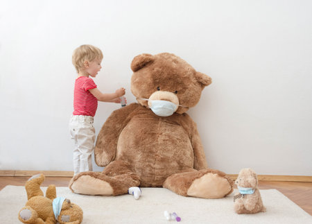 Child in home quarantine playing doctor in the balcony with his sick teddy bears wearing medical masks against viruses during coronavirus and flu outbreak. Illness COVID-2019 disease conceptの写真素材