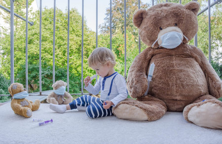 Child in home quarantine playing doctor in the balcony with his sick teddy bears wearing medical masks against viruses during coronavirus and flu outbreak. Illness COVID-2019 disease conceptの写真素材