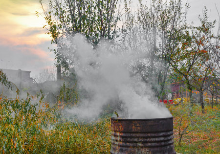 Autumn activity in garden, burning leaves, branches and dry grass in a old rusty barrel. Air pollution from farmers in the countrysideの写真素材