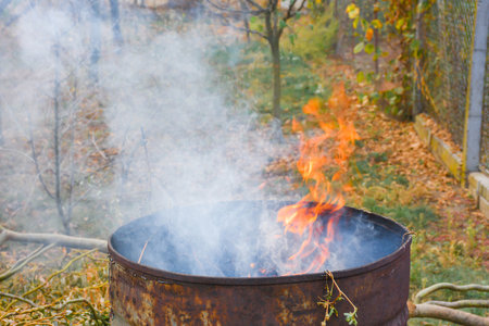 Autumn activity in garden, burning leaves, branches and dry grass in a old rusty barrel. Air pollution from farmers in the countrysideの写真素材