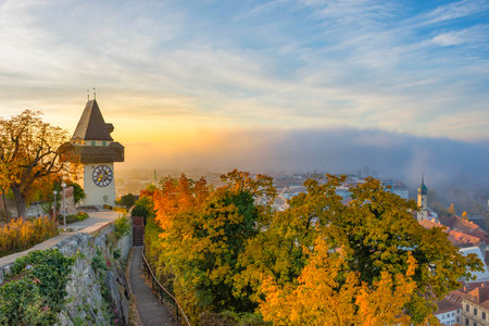 The famous clock tower on Schlossberg hill, in Graz, Styria region, Austria, at sunrise. Beautiful foggy morning over the city of Graz, in autumnの写真素材