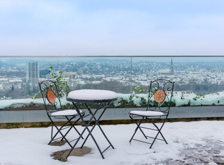 Table and chairs covered with snow on an empty terrace on Schlossberg hill, with beautiful view over the city of Graz,Styria region,Austria, in winterの写真素材