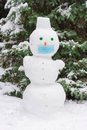 Cute snowman outdoor in the park on a snowy winter day, wearing a medical mask because of Coronavirus Covid 19 new reality and normal lifeの写真素材
