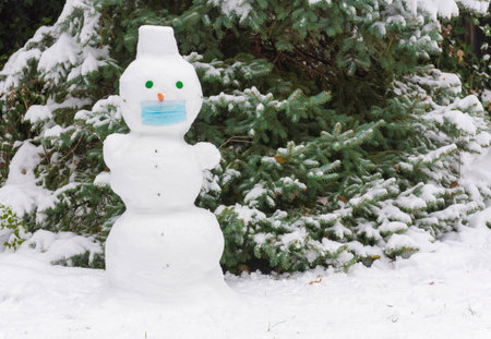 Cute snowman outdoor in the park on a snowy winter day, wearing a medical mask because of Coronavirus Covid 19 new reality and normal lifeの写真素材