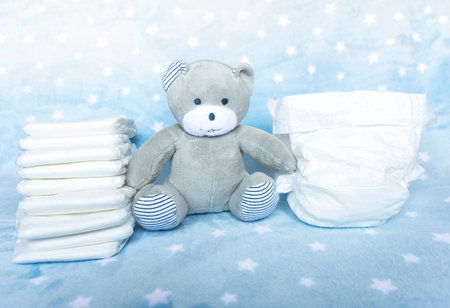 Stack of white disposable diapers for little babies on blue background with stars and cute teddy bear. Selective focusの写真素材
