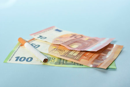 Cigarettes and money on blue background. Euro banknotes and coins, cost of smoking, cigarette price concept. Selective focusの写真素材