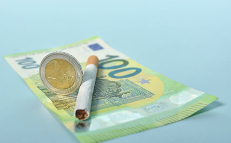 Cigarettes and money on blue background. Euro banknotes and coins, cost of smoking, cigarette price concept. Selective focusの写真素材