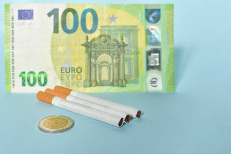 Cigarettes and money on blue background. Euro banknotes and coins, cost of smoking, cigarette price concept. Selective focusの写真素材