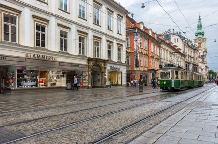 Graz/Austria - June 22, 2019: Herrengasse street with shops and green tram and Parish Church (Stadtpfarrkirche) in the background, in the city center of Graz, Styria region, Austria.のeditorial素材