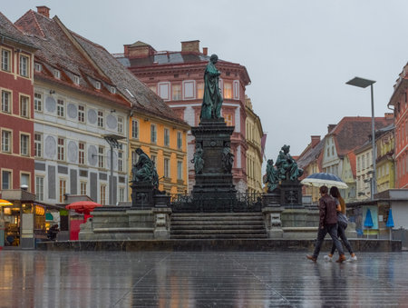 Graz/Austria - June 22, 2019: People with umbrella passing by Erzherzog Johann fountain at Hauptplatz (main square) in a rainy day, in Graz, Styria region, Austria.のeditorial素材