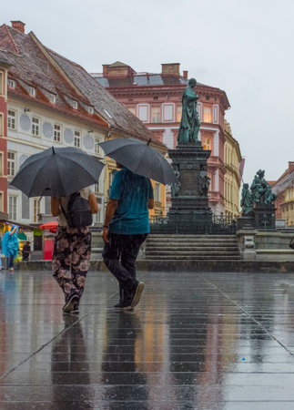 Graz/Austria - June 22, 2020: People with umbrella passing by Erzherzog Johann fountain at Hauptplatz (main square) in a rainy day, in Graz, Styria region, Austria.のeditorial素材