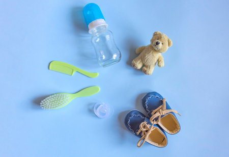 Baby care accessories, newborn baby pacifier, comb and hair brush, bottle, little boy shoes and toy on a blue background. Wish list or shopping overview for pregnancy, baby shower concept.の写真素材