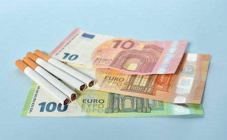 Cigarettes and money on blue background. Euro banknotes and coins, cost of smoking, cigarette price concept. Selective focusの写真素材