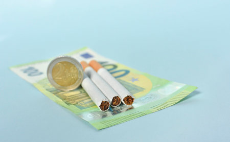 Cigarettes and money on blue background. Euro banknotes and coins, cost of smoking, cigarette price concept. Selective focusの写真素材